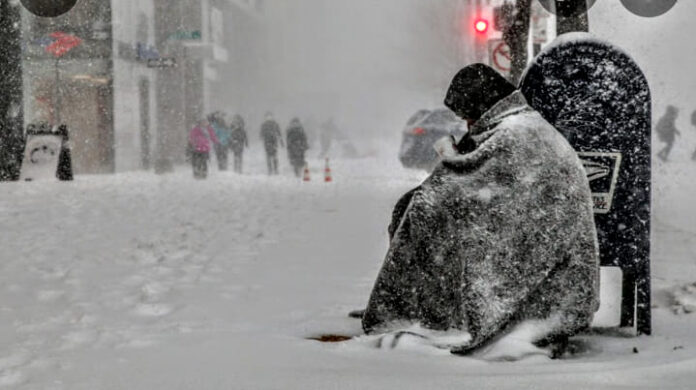 homeless person sitting on the street covered in snow