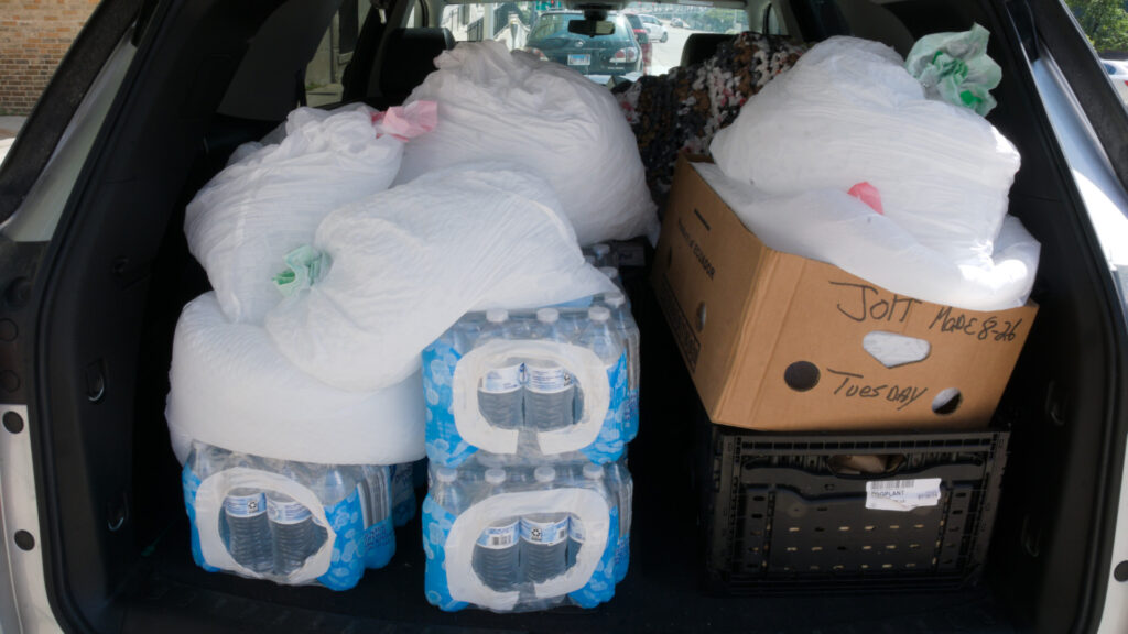 Trunk of care filled with water bottles, food, and bags of ice.